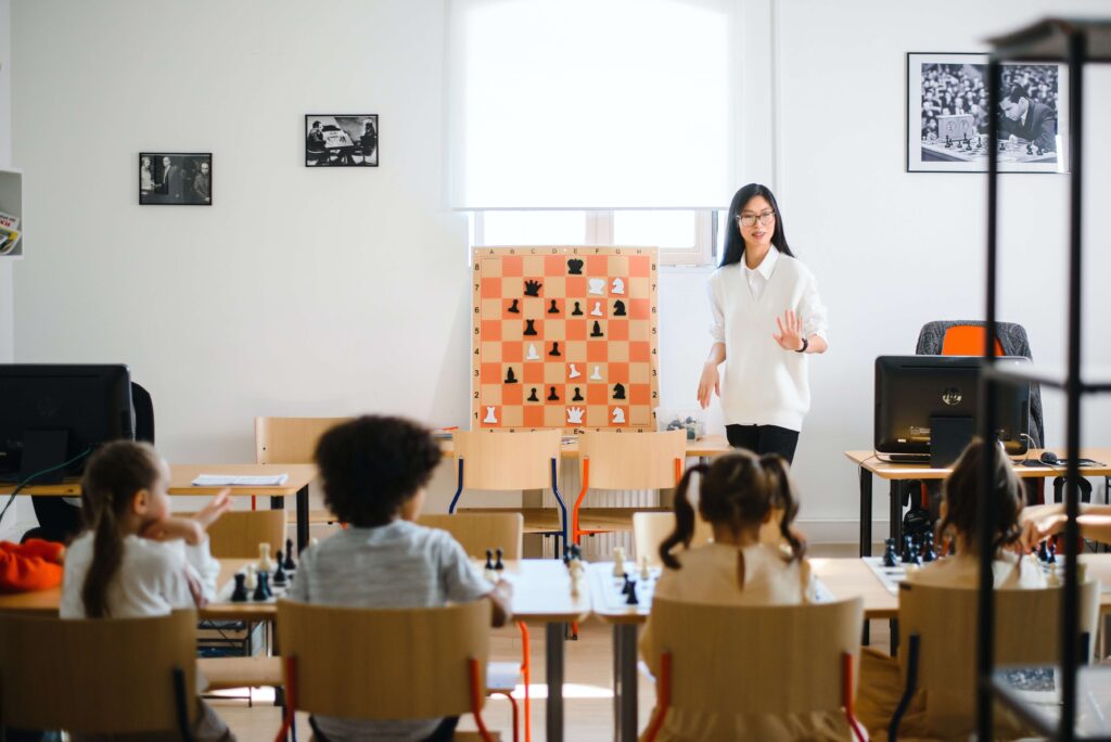 A woman teaching chess to a group of five children